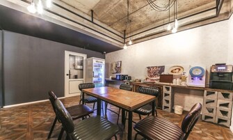 A dining area with a wooden table and black leather chairs, a refrigerator, and a coffee machine.