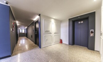 A long, narrow hallway with a polished floor, white doors, and a fire extinguisher on the right.