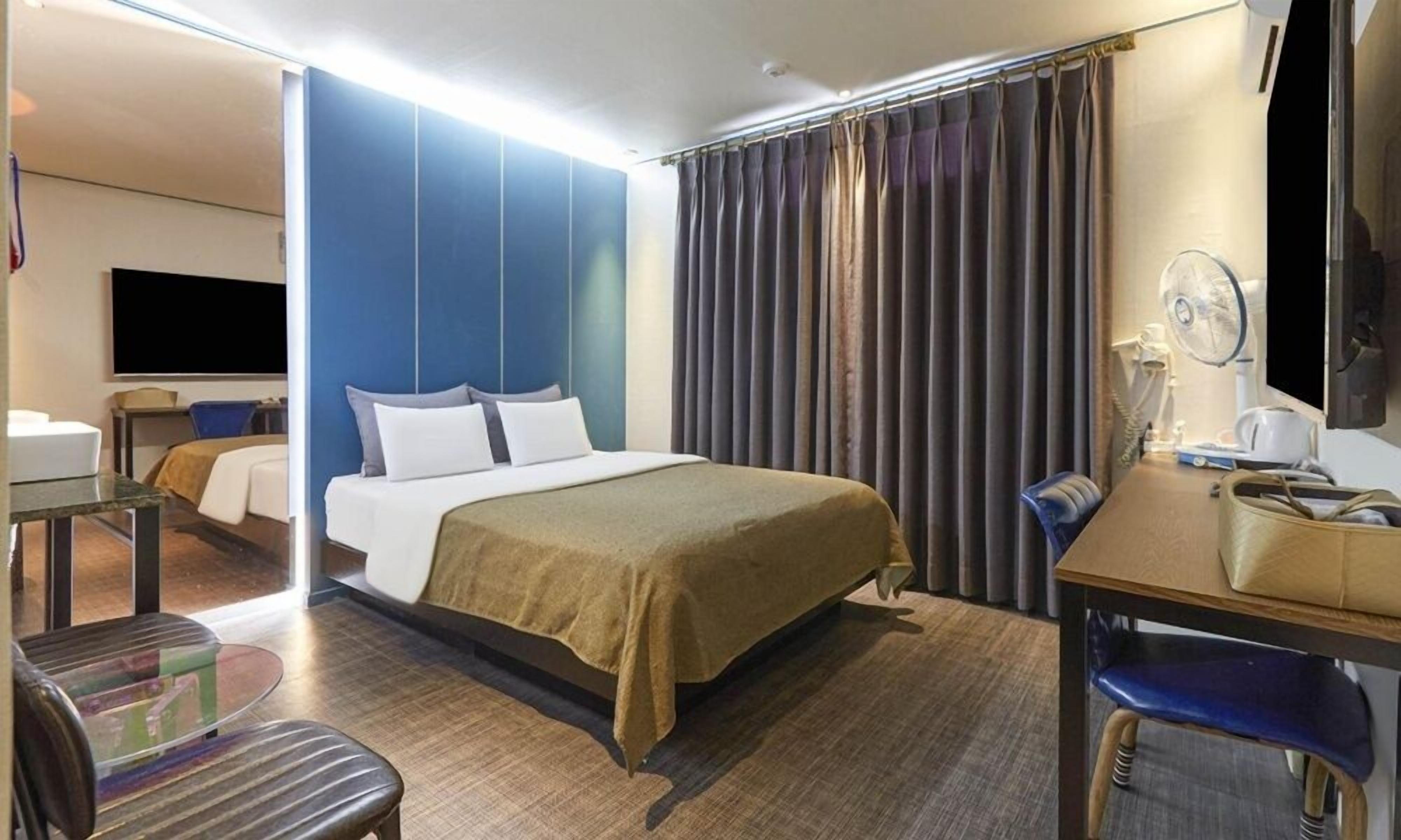 A hotel room with a bed, a desk, a chair, a TV, and a window with curtains.