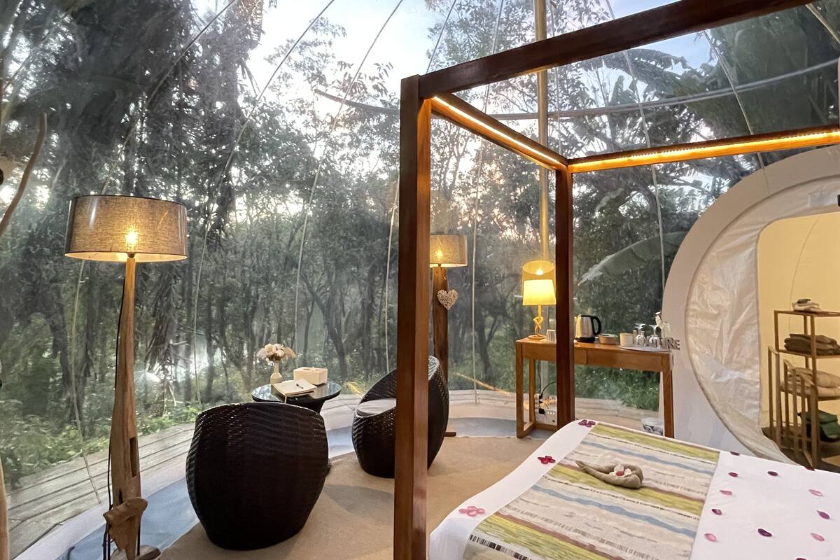 A cozy room with a large glass window, wooden furniture, and a view of a forest.