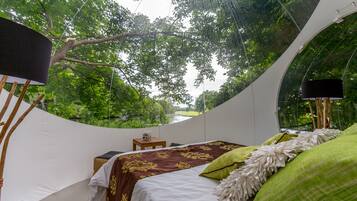 A circular room with a bed, a lamp, and a view of lush greenery.
