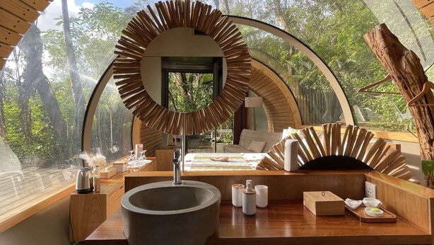 Un baño moderno con un espejo grande, techo de madera y vistas al bosque.