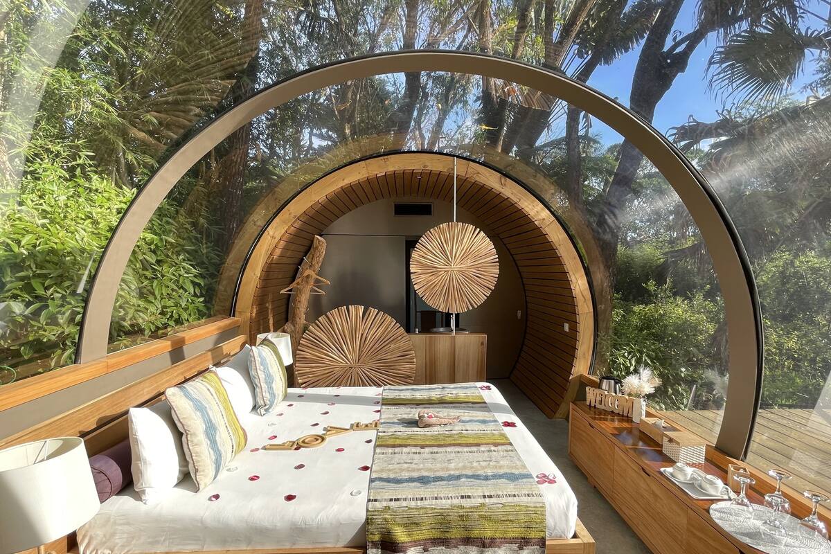 A cozy, circular room with a bed, wooden furniture, and a view of lush greenery.