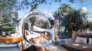 Una habitación cúpula transparente con cama, sofá y una mesa con hervidor y tazas.