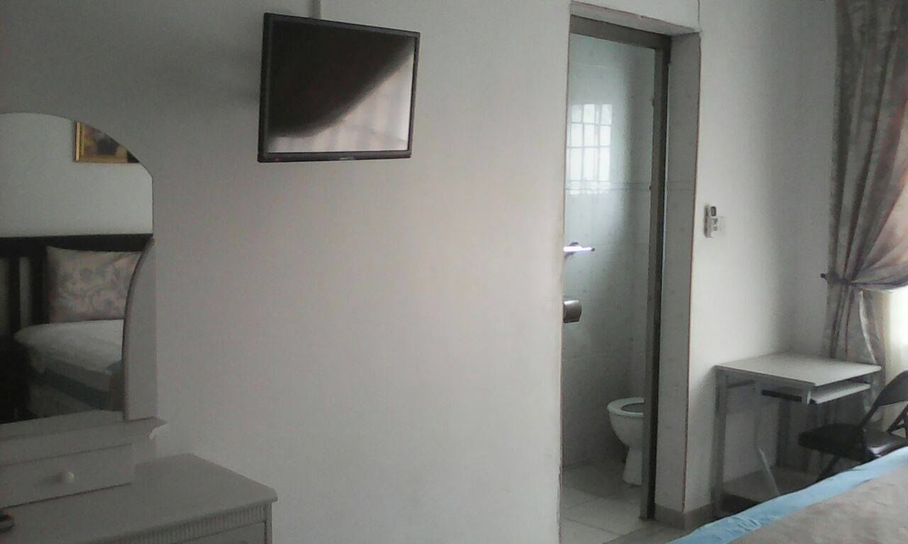 A hotel room with a bed, a desk, a chair, a TV, and a bathroom visible through an open door.