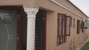 Un edificio con fachada color beige, una columna blanca prominente y una puerta con ventanal.
