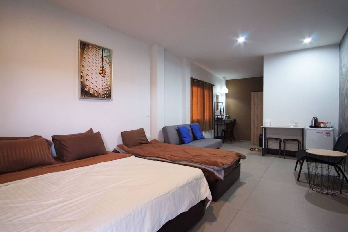 A hotel room with two beds, a sofa, a dining area, and a small kitchenette.
