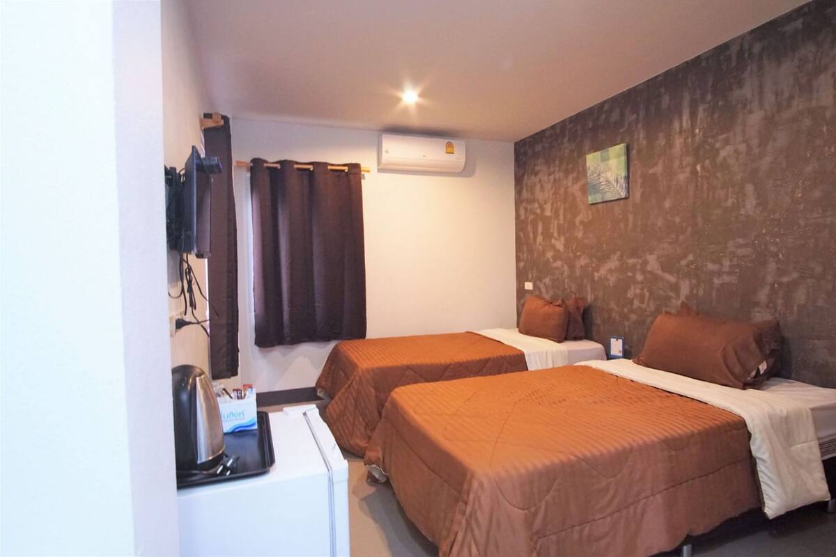 A hotel room with two beds, a coffee machine, a small table, and an air conditioning unit.