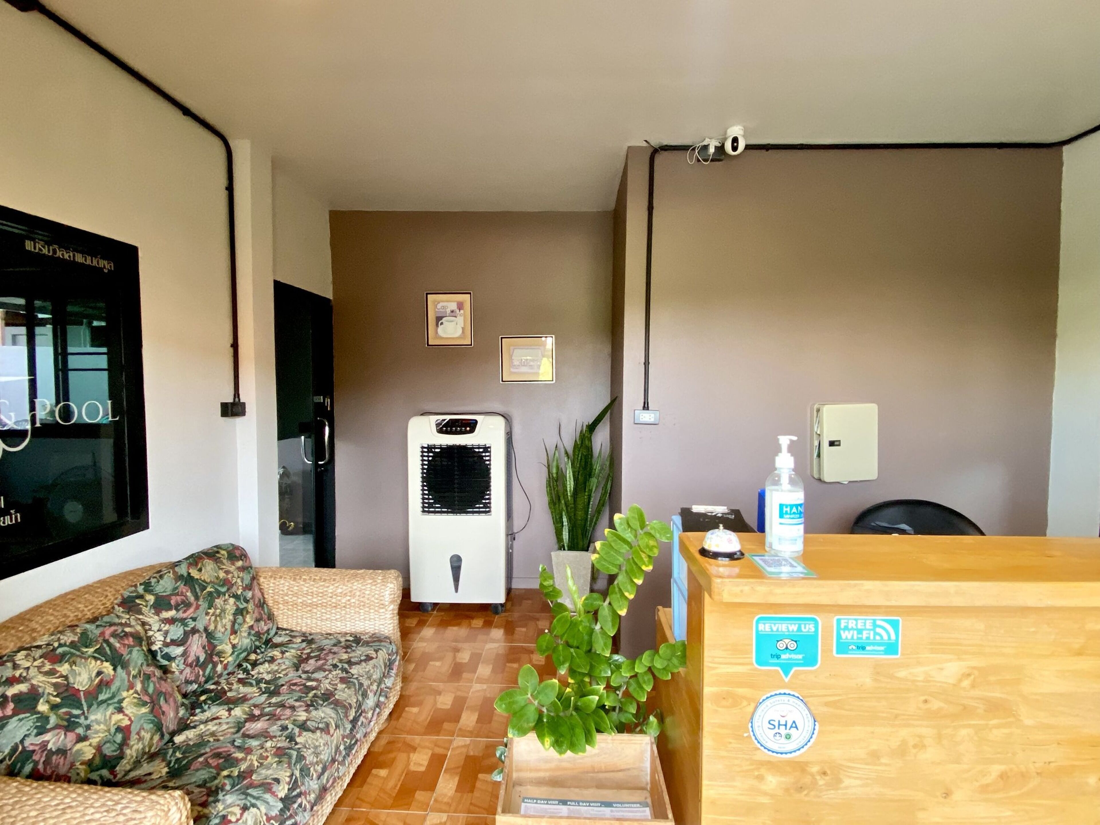 A reception area with a wooden desk, a sofa, a wall-mounted air conditioner, and a potted plant.