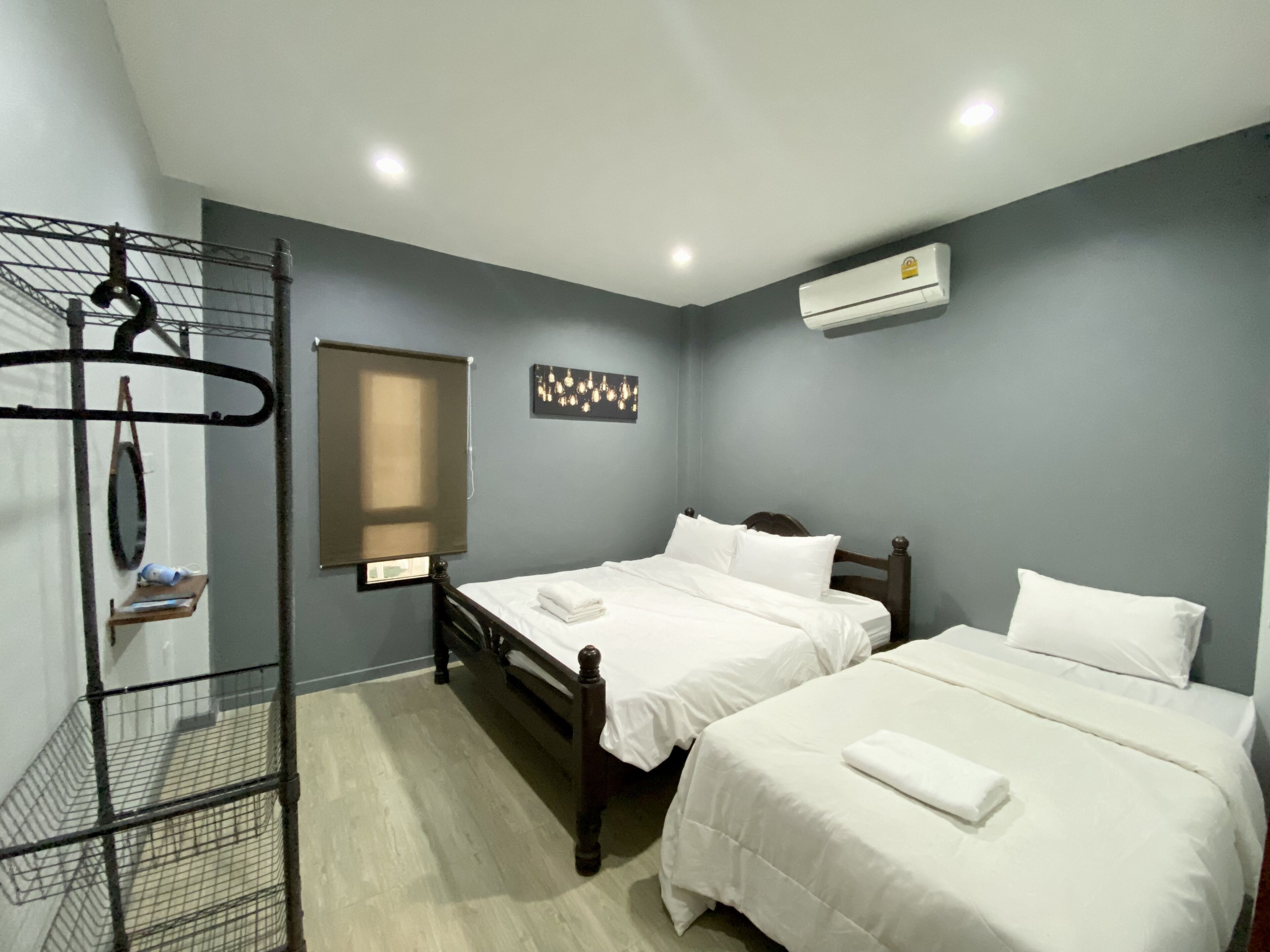 A hotel room with two beds, a metal rack, a window with blinds, and an air conditioning unit.