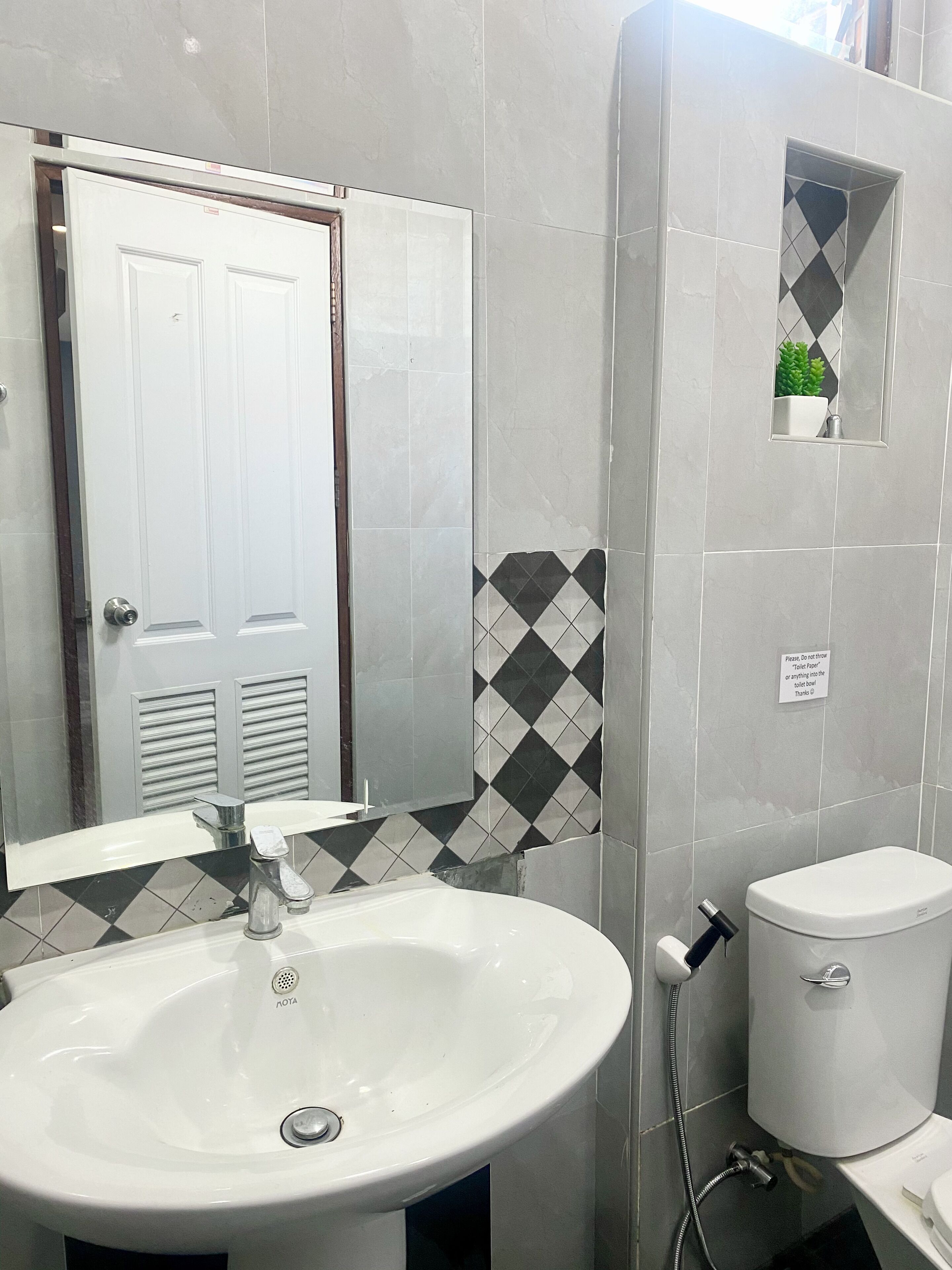 Ein Badezimmer mit einem weißen Waschbecken, einer Toilette und einer Dusche. Eine Tür mit einem Spiegel darüber, und ein Schild an der Wand.
