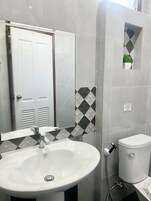 Ein Badezimmer mit einem weißen Waschbecken, einer Toilette und einer Dusche. Eine Tür mit einem Spiegel darüber, und ein Schild an der Wand.