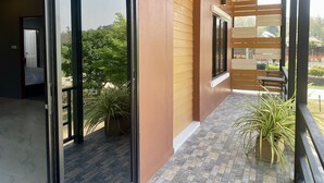 A covered balcony with a view of greenery, a tiled floor, and a door leading to a room. - Maerim Villa & Pool (Mae Rim)