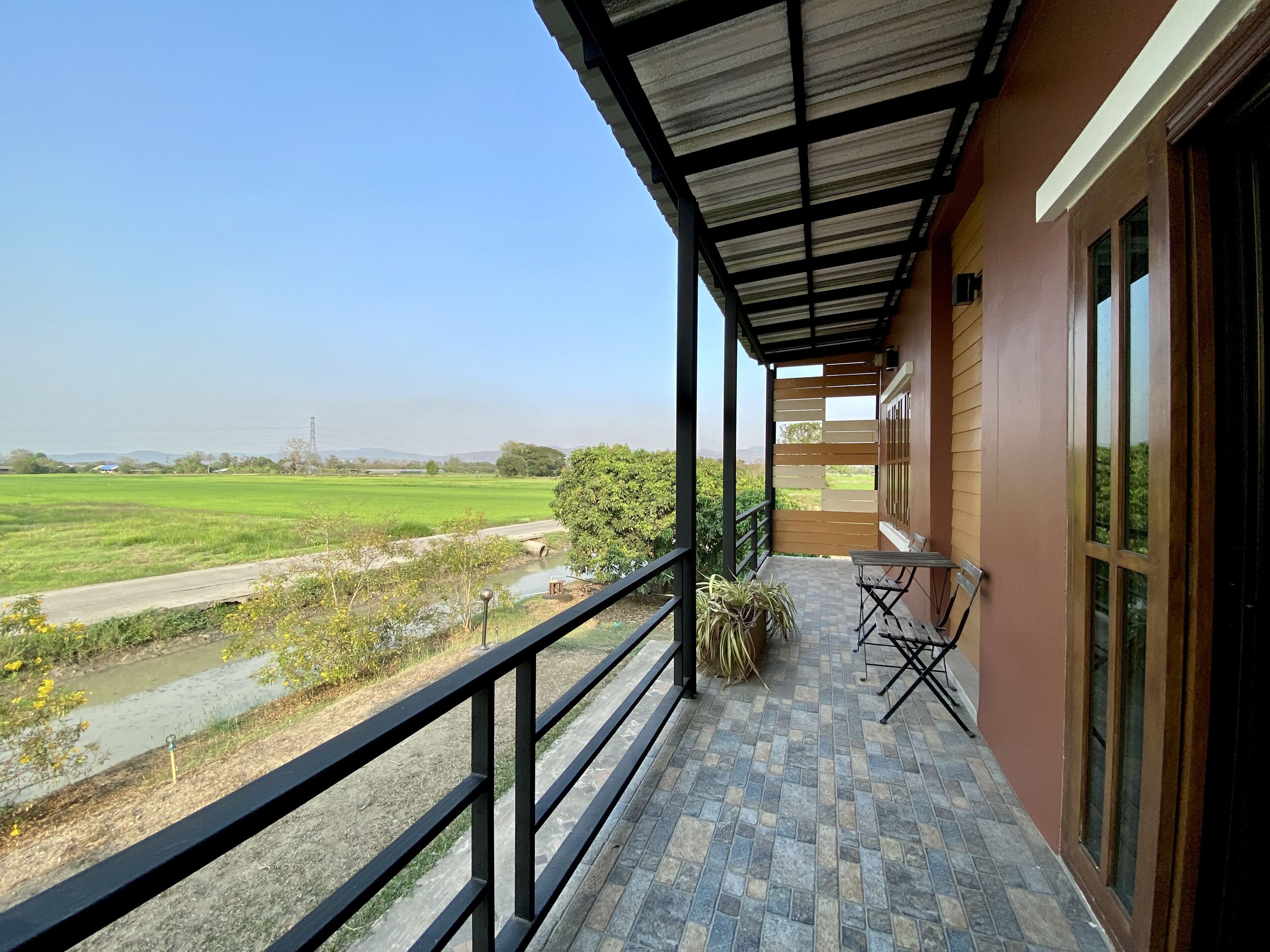 A balcony with a view of a green field and a river.