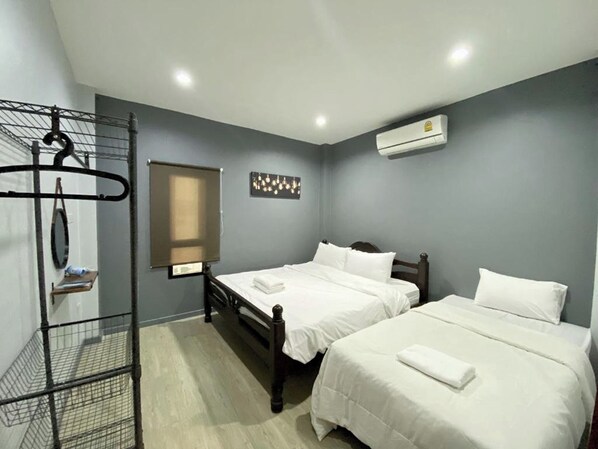 A hotel room with two single beds, a metal rack with clothes, a window, and an air conditioning unit.