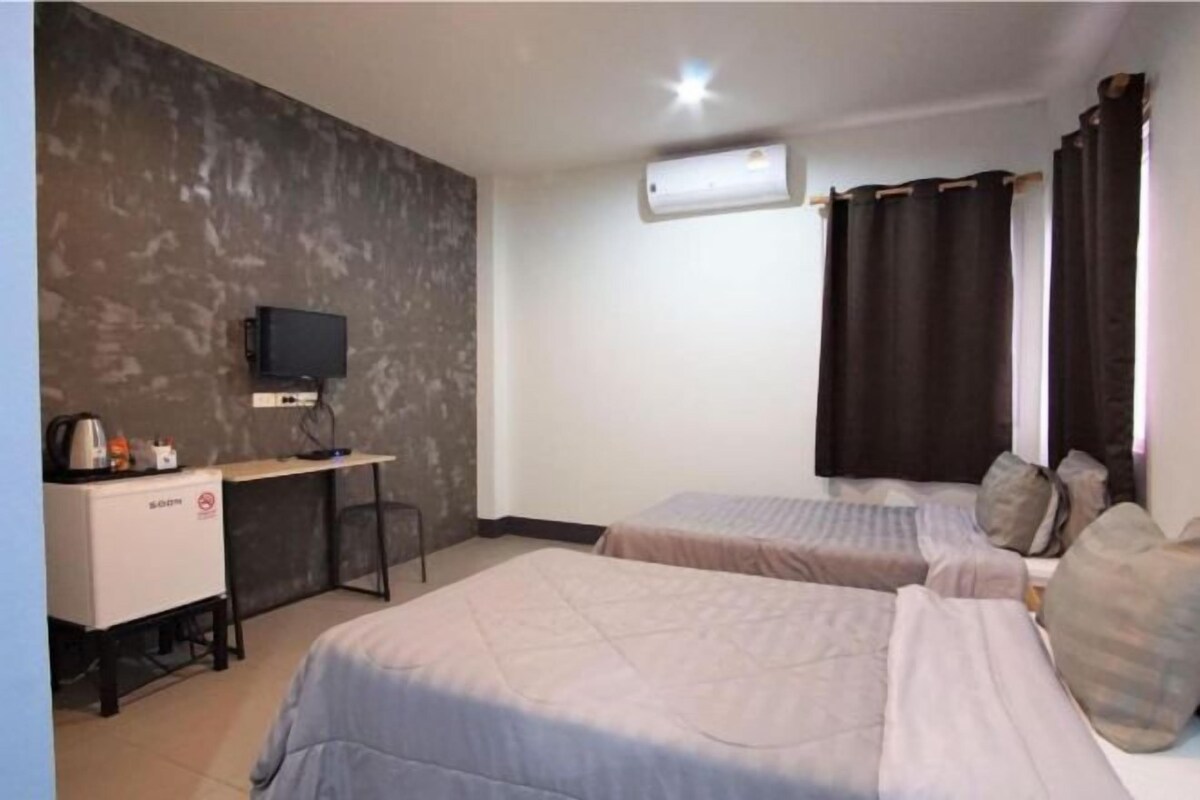 Een hotelkamer met twee bedden, een bureau met een televisie en een airconditioning.