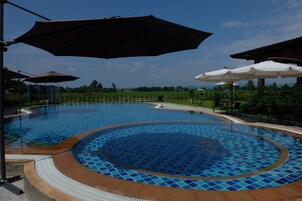 Una piscina con diseños azules y marrones en mosaico, rodeada de mobiliario de exterior y sombrillas.