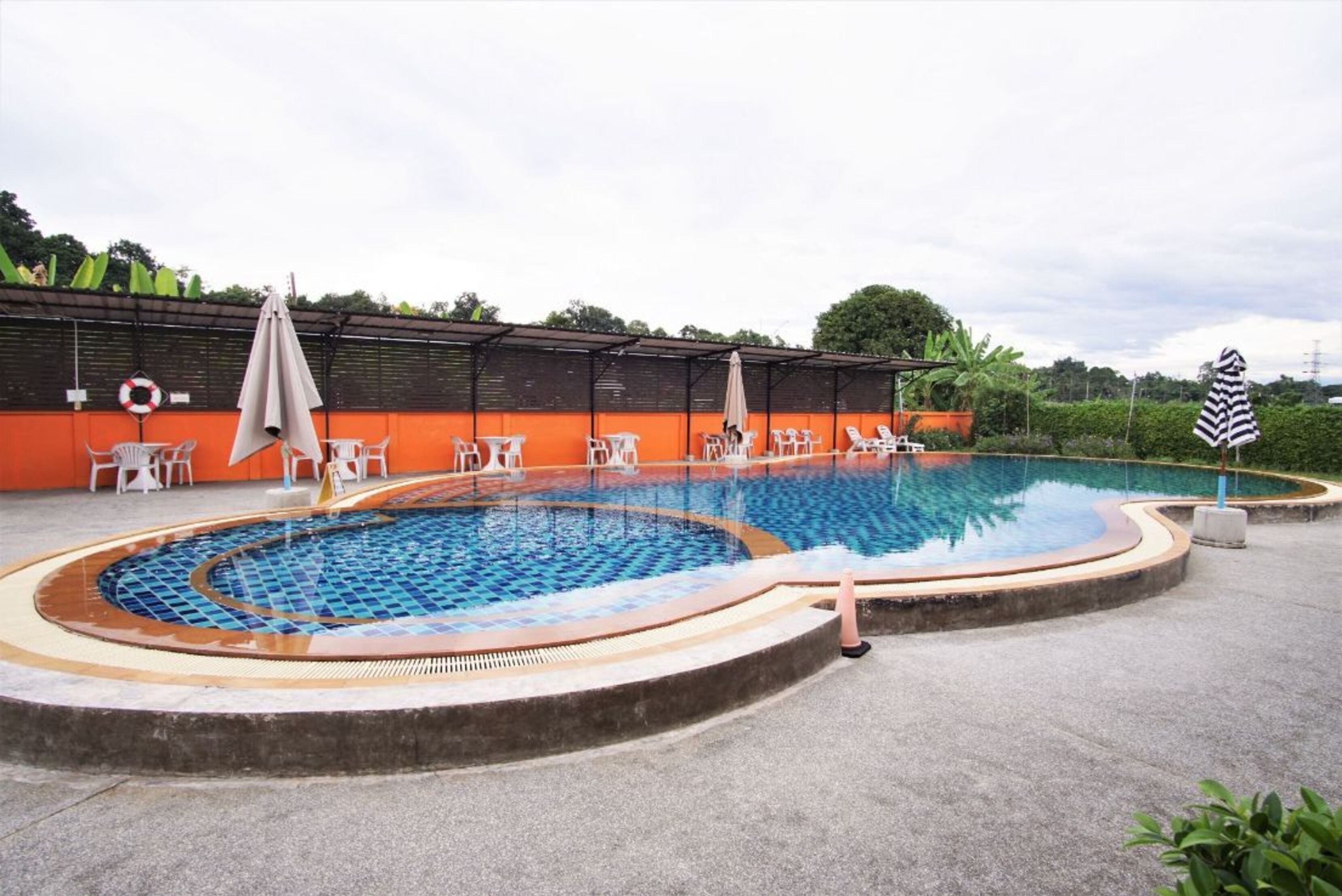 A swimming pool with a tiled edge, surrounded by lounge chairs and umbrellas.