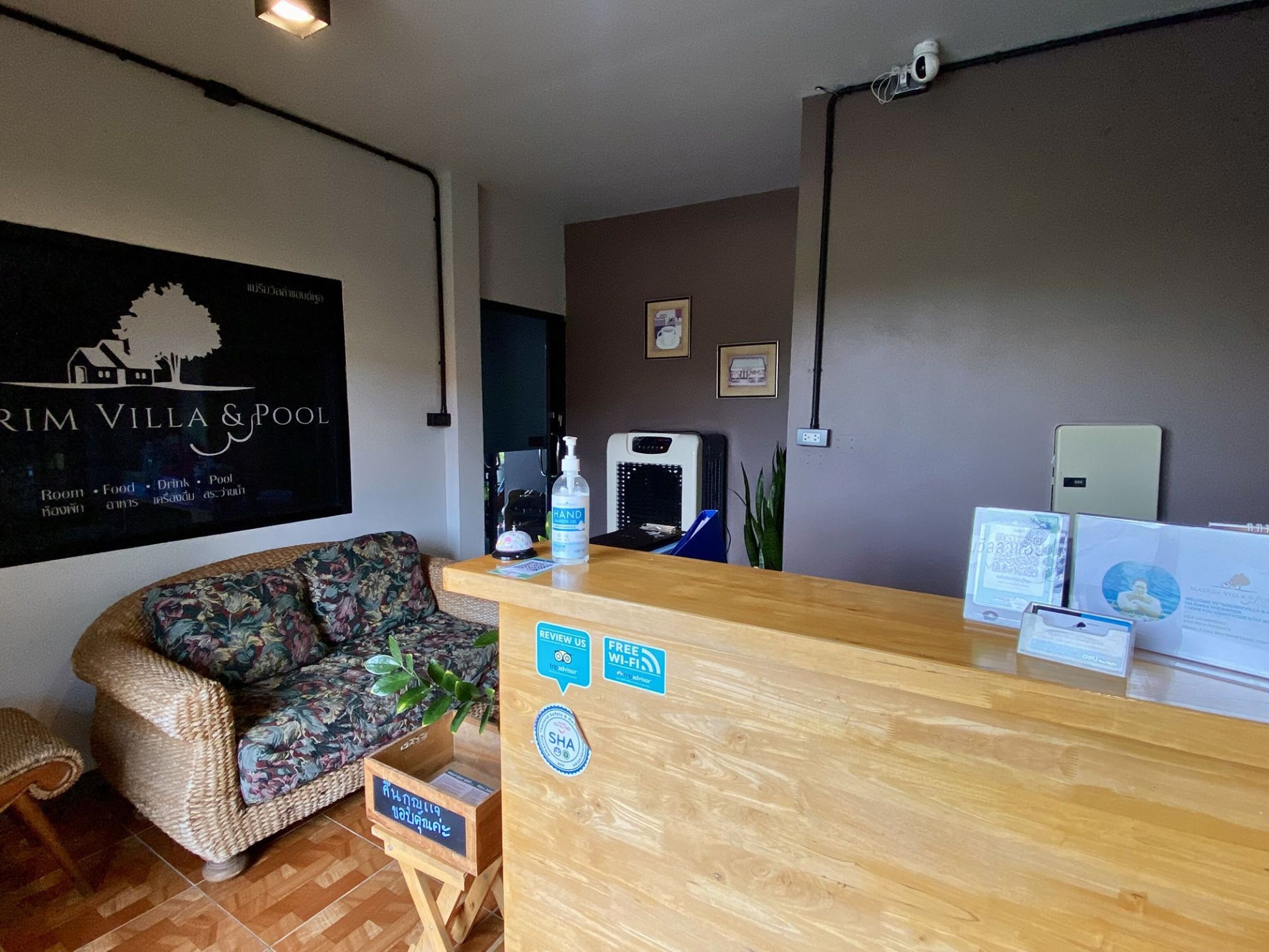 Un espace d’accueil comprenant un comptoir en bois, un canapé à motifs floraux, un panneau fixé au mur et un distributeur de gel hydroalcoolique.