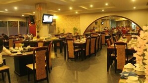 Un restaurant spacieux, doté de nombreuses tables et chaises, d’un téléviseur fixé au mur et d’un mur en pierre en arrière-plan.