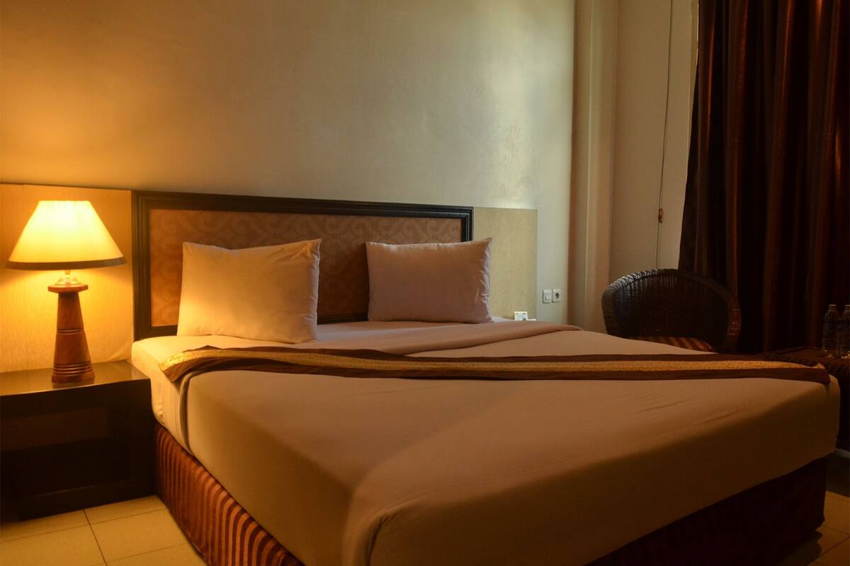 A neatly made bed with a headboard, a bedside lamp, and a chair.