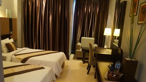Une chambre d’hôtel avec deux lits, un bureau, une chaise, une lampe et une petite table sur laquelle se trouvent une bouteille et des verres.