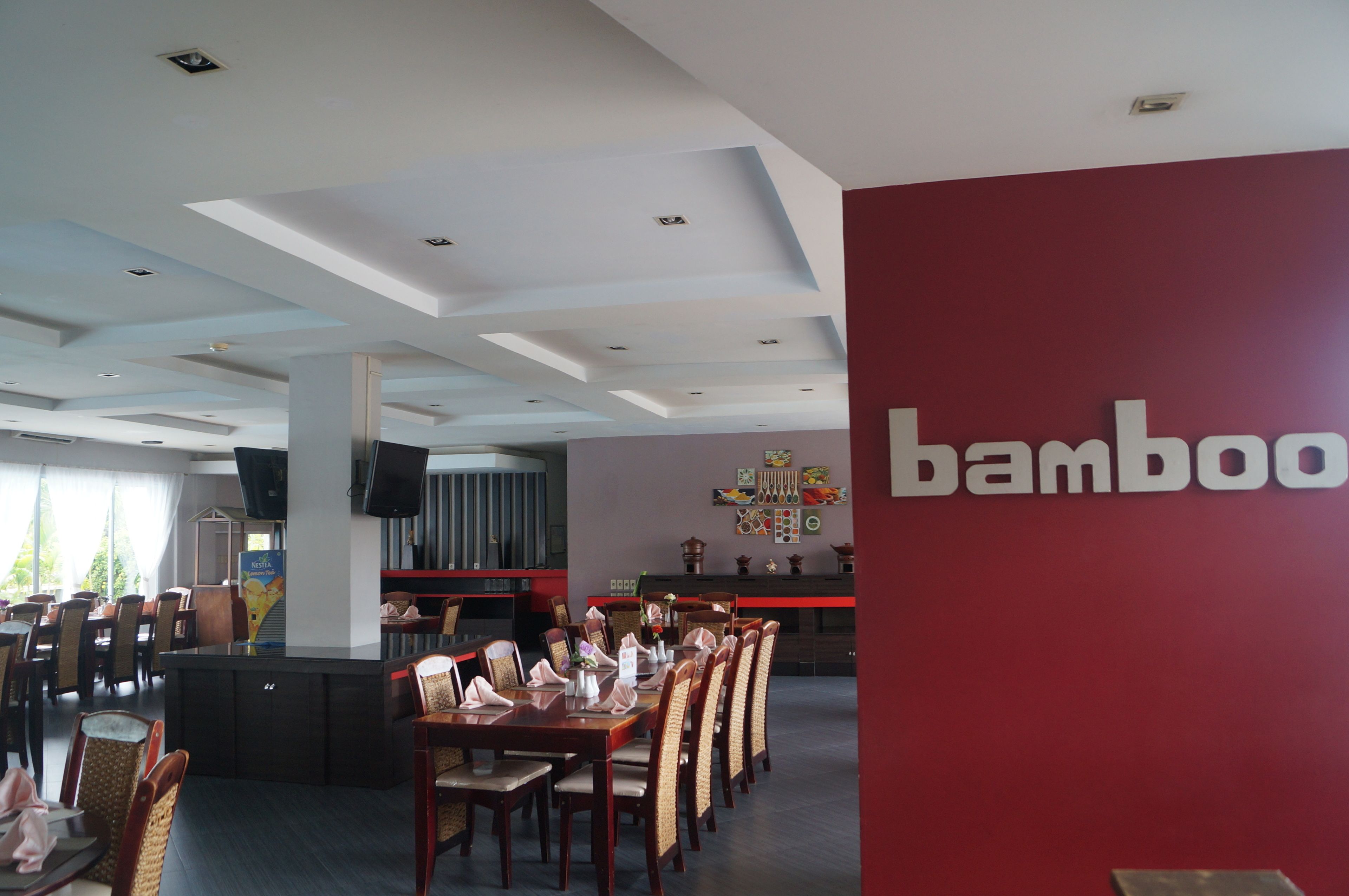 Ein Restaurant mit roter Wand, auf der das Wort 'bamboo' steht. Tische und Stühle sind für das Essen bereitgestellt.