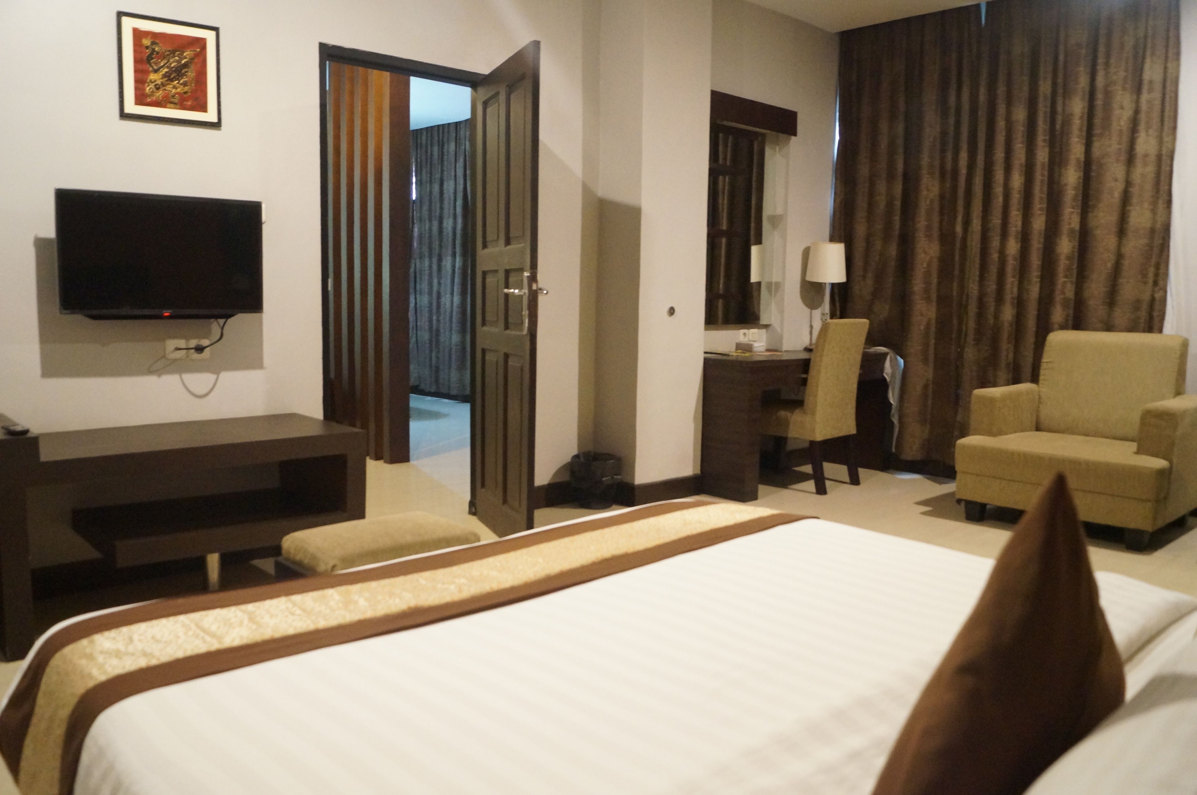A hotel room with a bed, a desk, a chair, a television, and a door leading to another room.