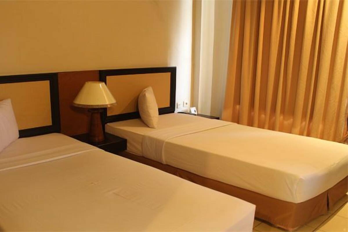 A hotel room with two single beds, a nightstand with a lamp, and a window with curtains.