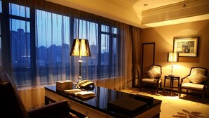 Habitación de hotel con un ventanal grande, un escritorio con lámpara, dos sillas y piso alfombrado.