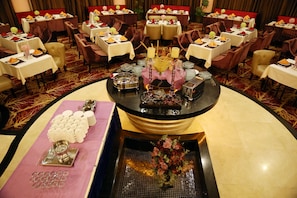 Une salle à manger élégante, avec plusieurs tables dressées pour le service, une composition décorative centrale et un arrangement floral placé sur une surface réfléchissante.