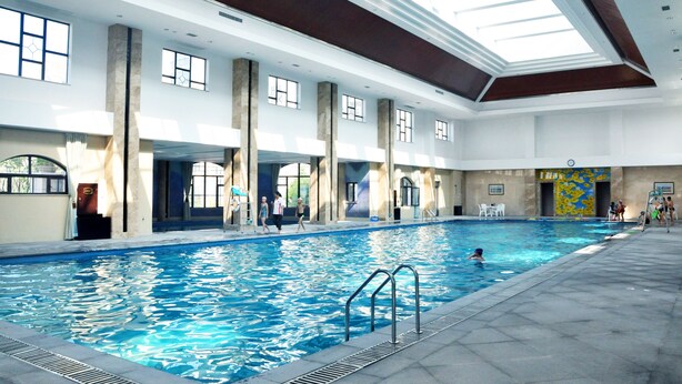 Una piscina interior con agua cristalina, ventanas amplias y un techo alto.
