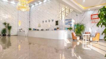Een hotellobby met een receptiebalie, een zithoek en decoratieve planten.