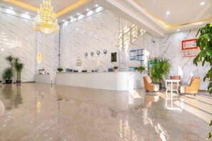 Un vestíbulo de hotel con mostrador de recepción, zona de estar y plantas decorativas.