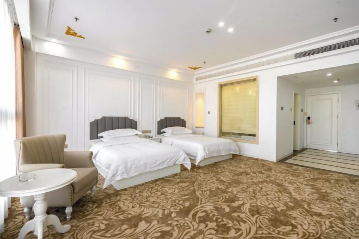 A hotel room with two beds, a small round table, a chair, and a patterned carpet.