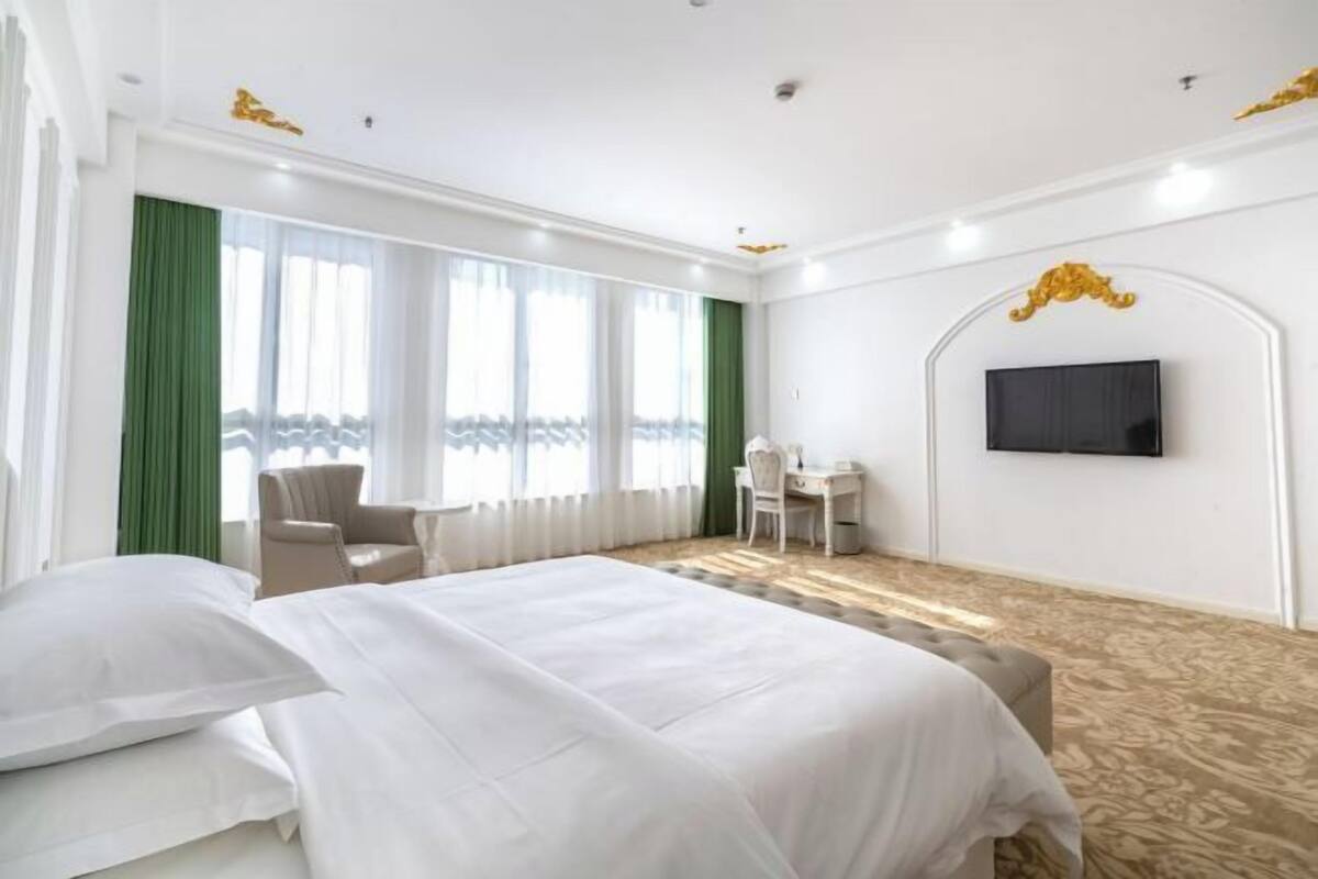 A hotel room with a large bed, a desk, a chair, and a television on the wall.