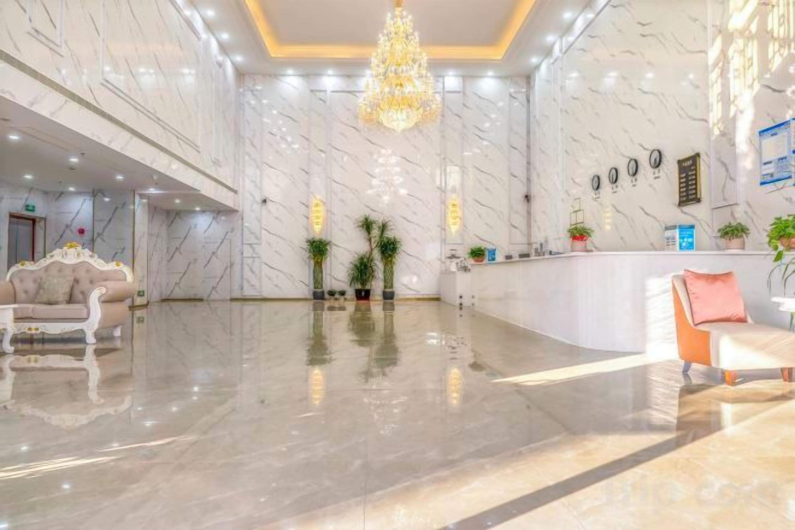 A hotel lobby with marble walls, a reception desk, and a chandelier.