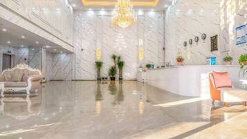 A hotel lobby with marble walls, a reception desk, and a chandelier.