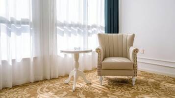 Een kamer met een kamerbreed tapijt, een crème kleur fauteuil, een kleine witte tafel en dunne gordijnen.