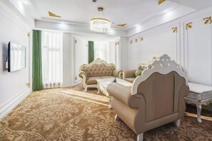 A room with a patterned carpet, a sofa, a chair, a small table, and a television on the wall.