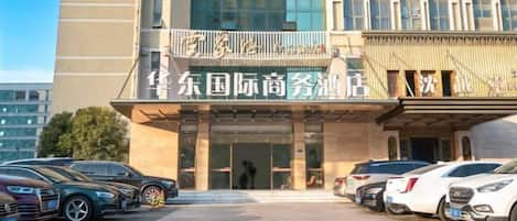 A hotel entrance with a modern facade, a covered entrance area, and several parked cars in front.