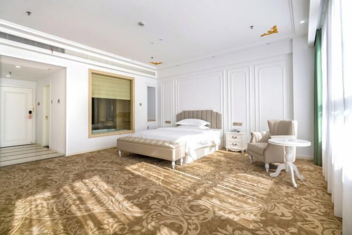 A hotel room with a large bed, a small desk, a chair, and a round table.
