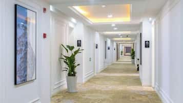 A hotel hallway with a carpeted floor, white walls, and framed artwork.