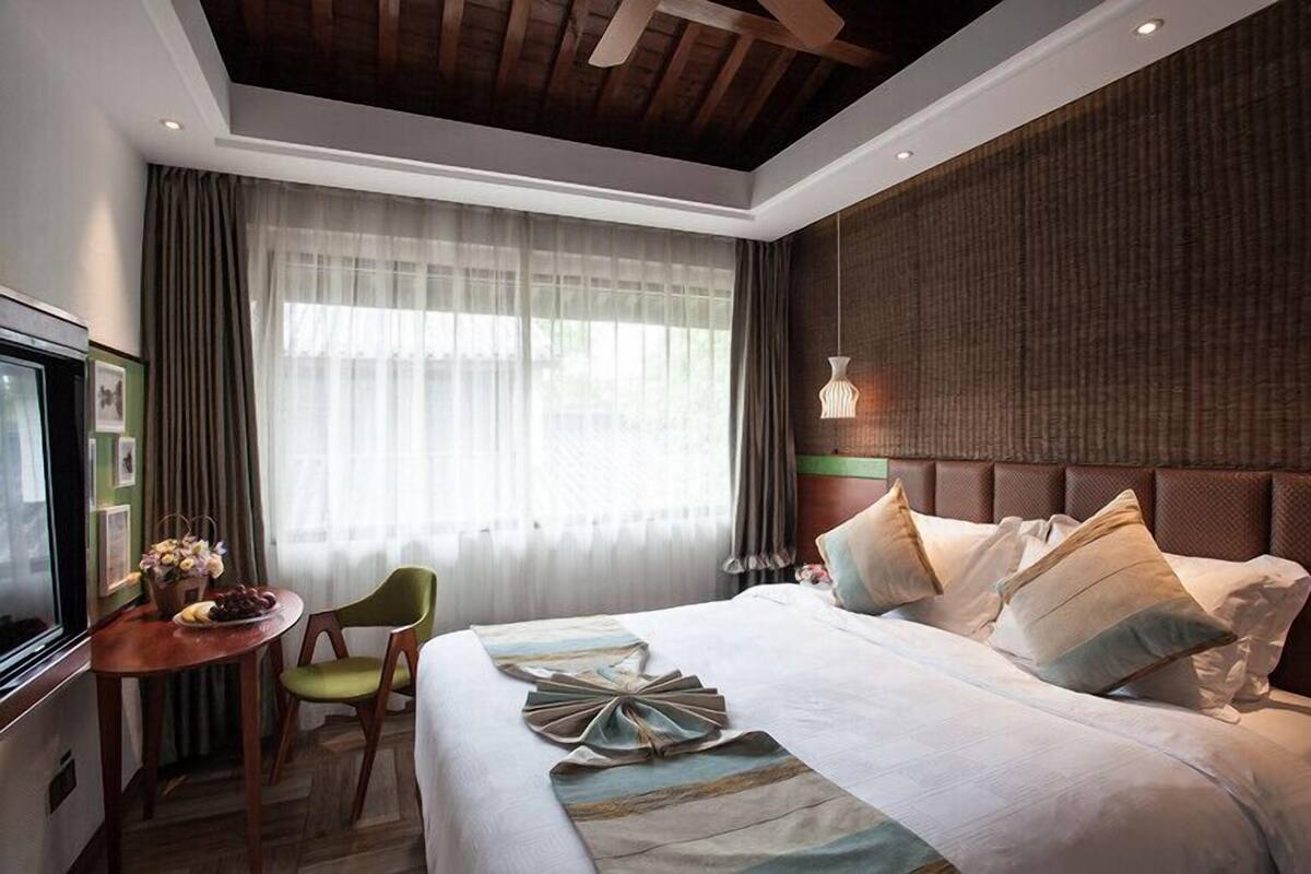 A hotel room with a large bed, a desk with a chair, a television, and a window with curtains.