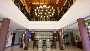 Vestíbulo de hotel con una suntuosa araña, una recepción y un techo alto.