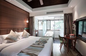 Une chambre d’hôtel moderne dotée d’un grand lit, d’une télévision, d’un balcon avec une chaise et d’un coin repas avec une table et des chaises.
