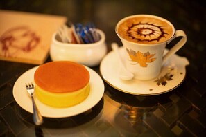 Une assiette à dessert avec un gâteau et une tasse de café agrémentée d’un motif en latte art.