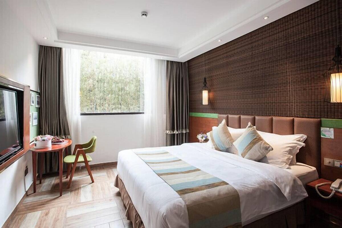 A hotel room with a large bed, a desk with a chair, a television, and a window with curtains.
