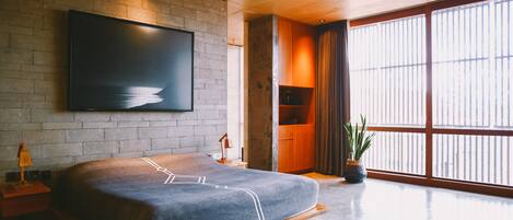 A modern bedroom with a large bed, a mounted TV, and a large window with curtains.