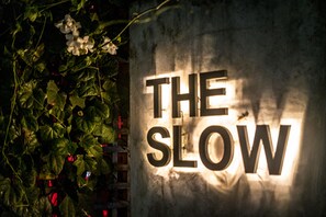 A sign with the words "THE SLOW" illuminated against a wall. - The Slow (Canggu)